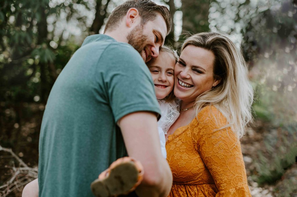 Mom and Dad holding daughter and cuddling together in the middle of Bush park in Salem Oregon. 