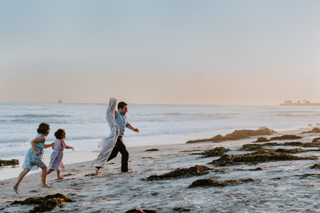Dad playing with daughters on the beach using movement to in family photos. 